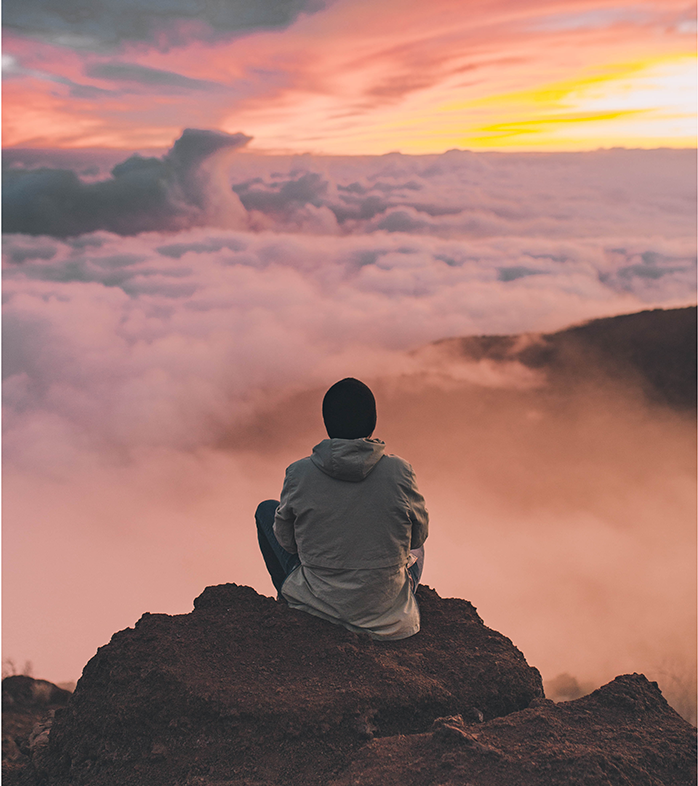 Eine Person sitzt auf einem Berg und schaut in die Wolken